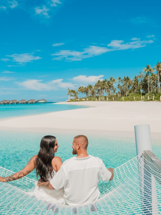 Couple sitting on a overwater hammock at Avani+ Fares Maldives Resort